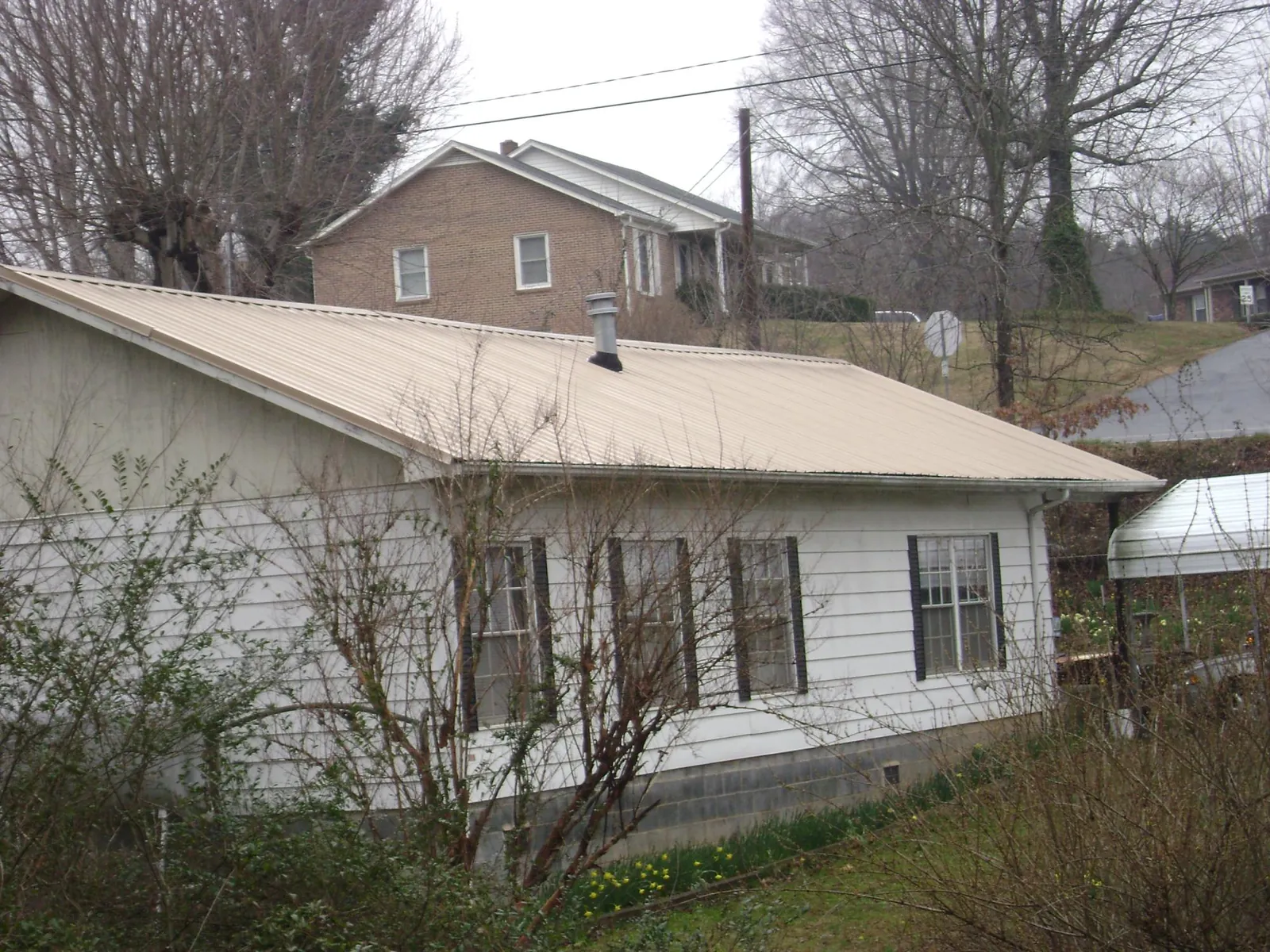 Tan metal roof on a white sided house set into a hillside — Commercial Roofing by Roofing Brothers in Deal
